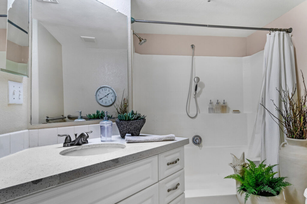 A bathroom with a bathtub shower, an analog clock, and sink with white cabinets and mirrors.
