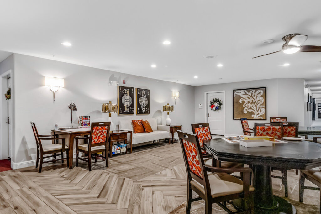 A sitting area with brown tables and red-patterned chairs, a white couch with orange throw pillows.