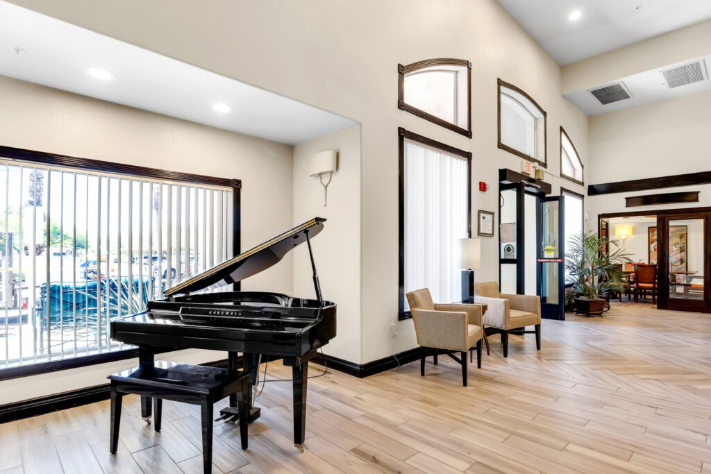 A lobby room with high ceilings, a black piano and two beige sofa chairs.