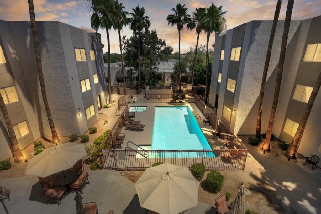 A view of the pool from above at dusk, with palm trees in front of it and buildings to the side, with lights on in each room at The Ranch Estates at Scottsdale.