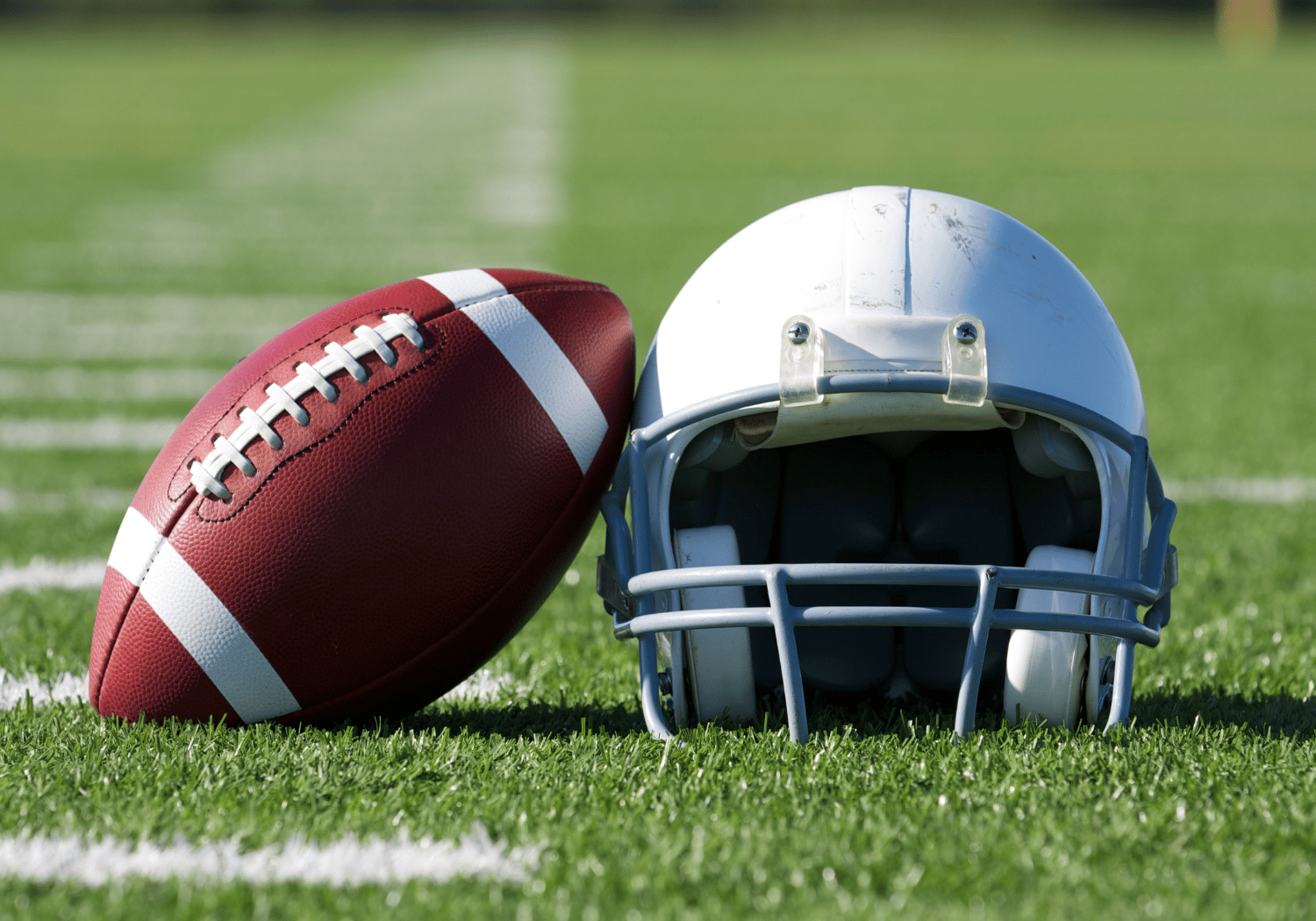 American football lies next to a white helmet on a green football field, ready for play.